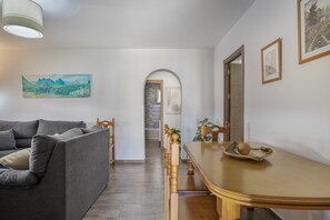 A modern living room with a grey sofa, wooden dining table, and a view of a mountain landscape through an archway.