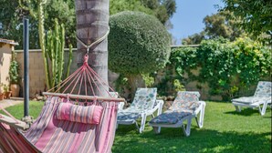 Un hamac est attaché à un arbre, entouré d’une pelouse bien entretenue et de chaises longues.