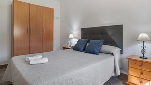 Une chambre à coucher comprenant un lit, une armoire, deux tables de chevet avec des lampes et une petite table de nuit.