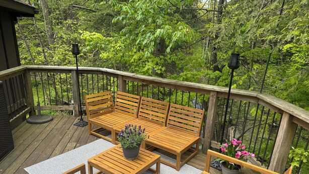 Une terrasse en bois avec un banc et des chaises, entourée d’une végétation luxuriante.