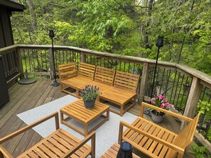 A wooden deck with a bench and chairs, surrounded by lush greenery.