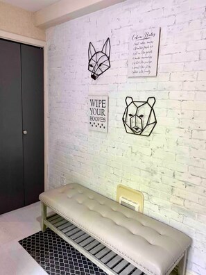A room with a white brick wall, a grey door, and a bench with a vintage radio.