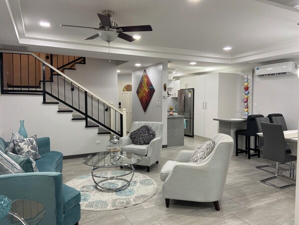 A modern living room with a staircase, a dining area, and a kitchen.
