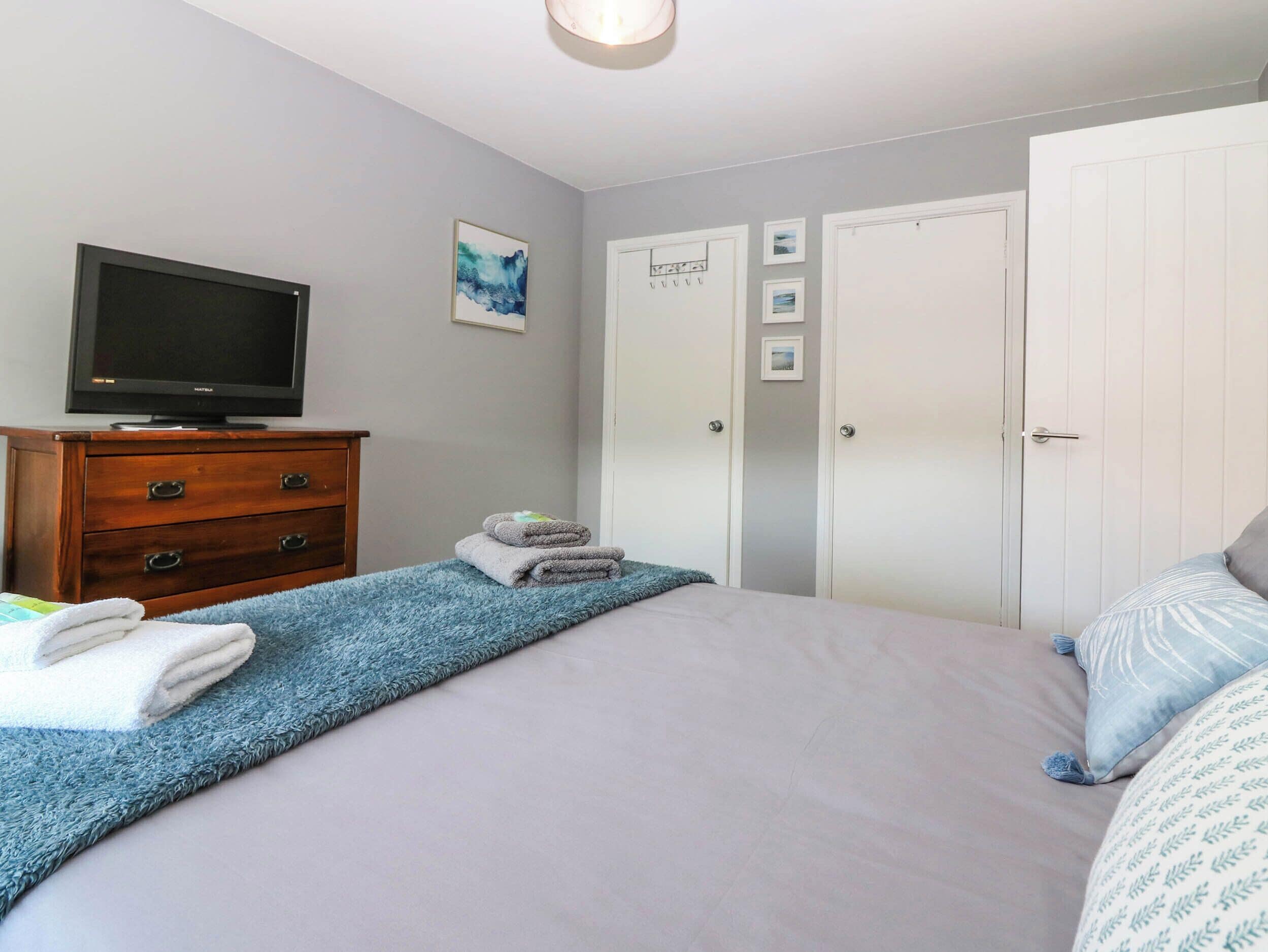 A bedroom with a bed, a TV on a dresser, a wardrobe, and a door with a sign.
