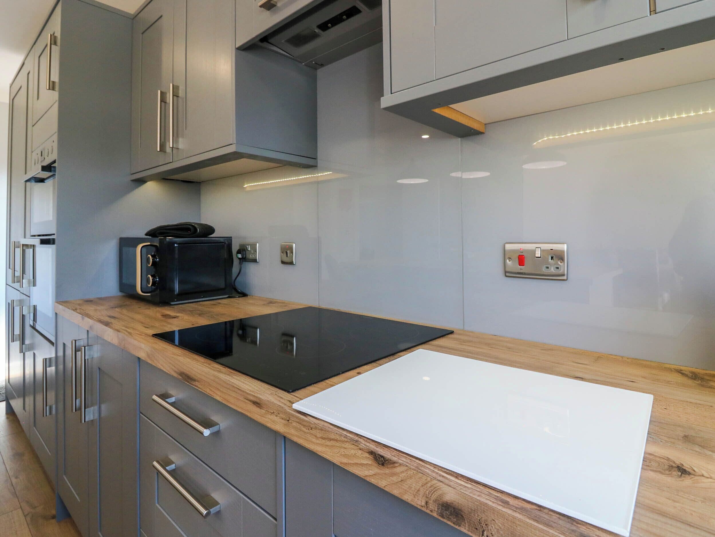 A modern kitchen with grey cabinets, a black induction cooktop, and a wooden countertop.