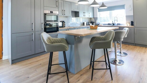 A modern kitchen with grey cabinets, a central island with bar stools, stainless steel appliances, and pendant lighting. - Fircroft (Perth)