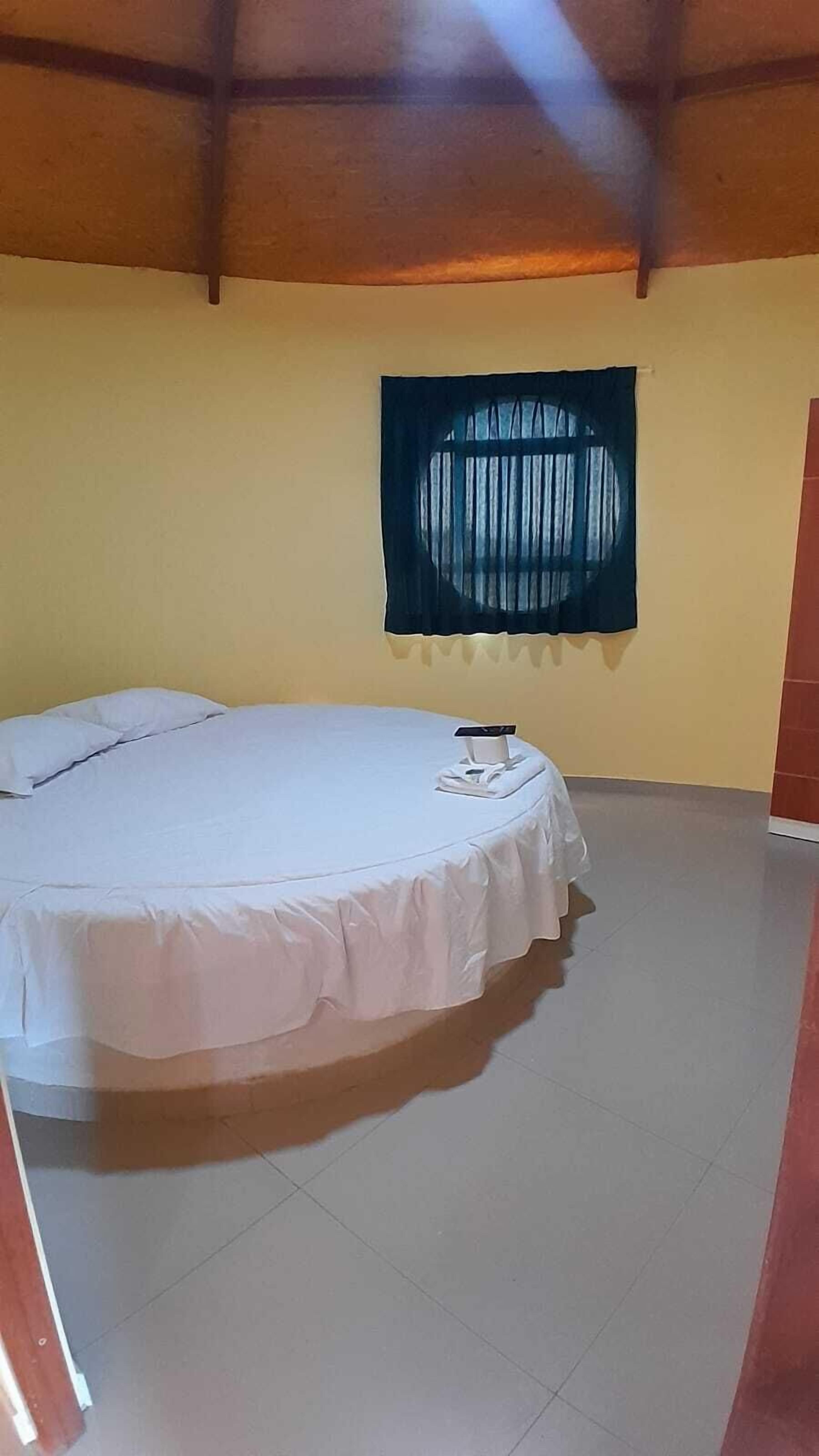 A single bed in a room with a plain yellow wall and a dark curtain.