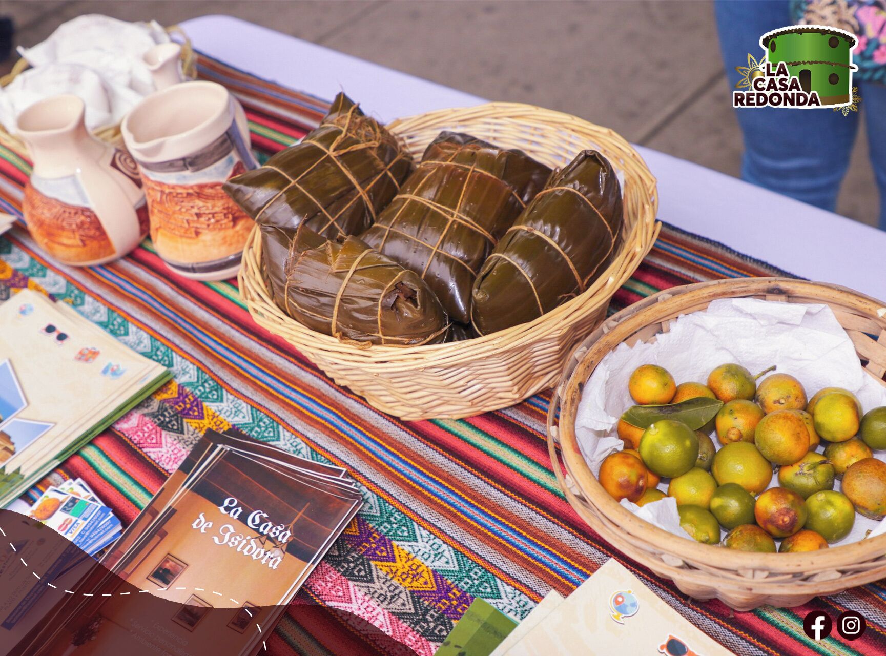 A table with tamales wrapped in leaves, a basket of limes, and a booklet titled "La Casa Redonda".