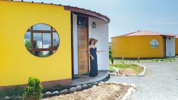 Un edificio amarillo con un ventanal circular y una puerta, rodeado por un camino de grava y pequeñas plantas.