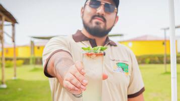 A person holding a tall glass with a drink, wearing a shirt with a logo, outdoors with buildings in the background.