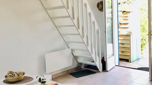 A modern interior with a white staircase, a dining area with a table and chairs, and a view of the outside through an open door. - At the foot of the dunes and the beach! Ideal for a quiet place (Barbâtre)