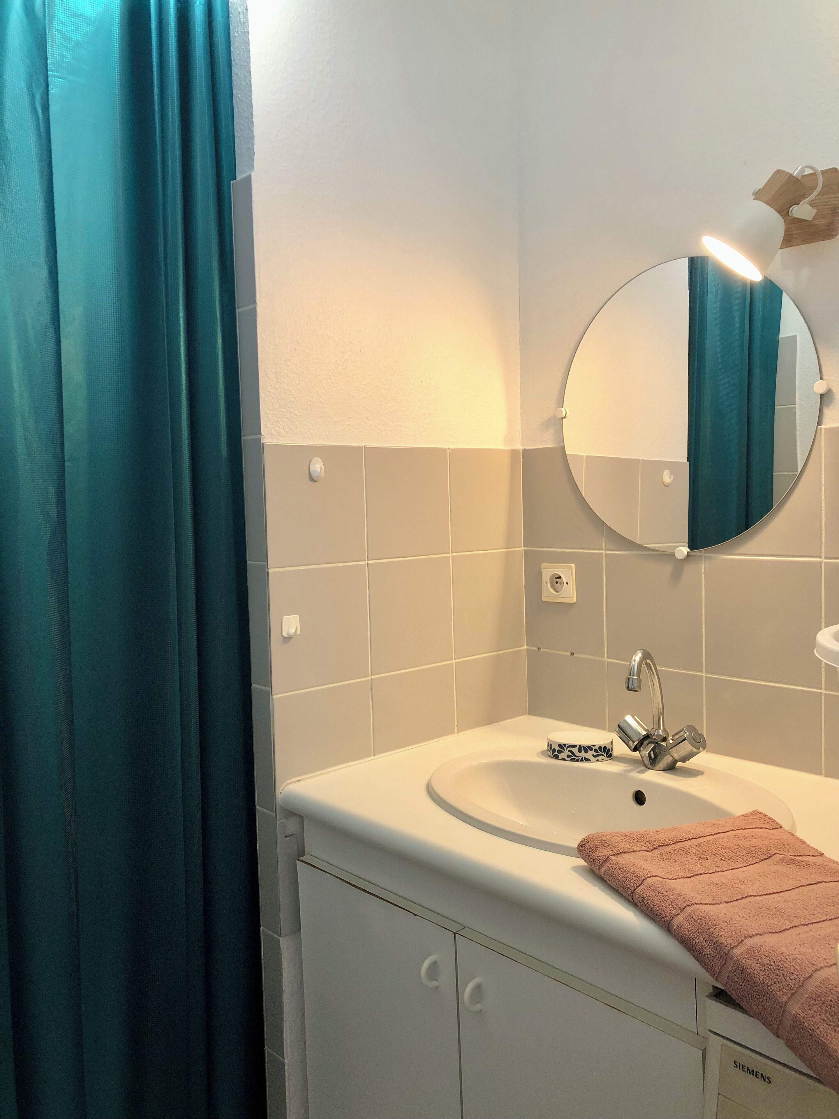 A bathroom with a white sink, a mirror, a towel, and a teal shower curtain.