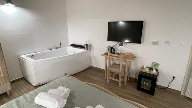 Une salle de bain moderne avec une baignoire, une chaise en bois, une petite table et un téléviseur fixé au mur.