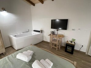Une salle de bain moderne avec une baignoire, une chaise en bois, une petite table et un téléviseur fixé au mur.