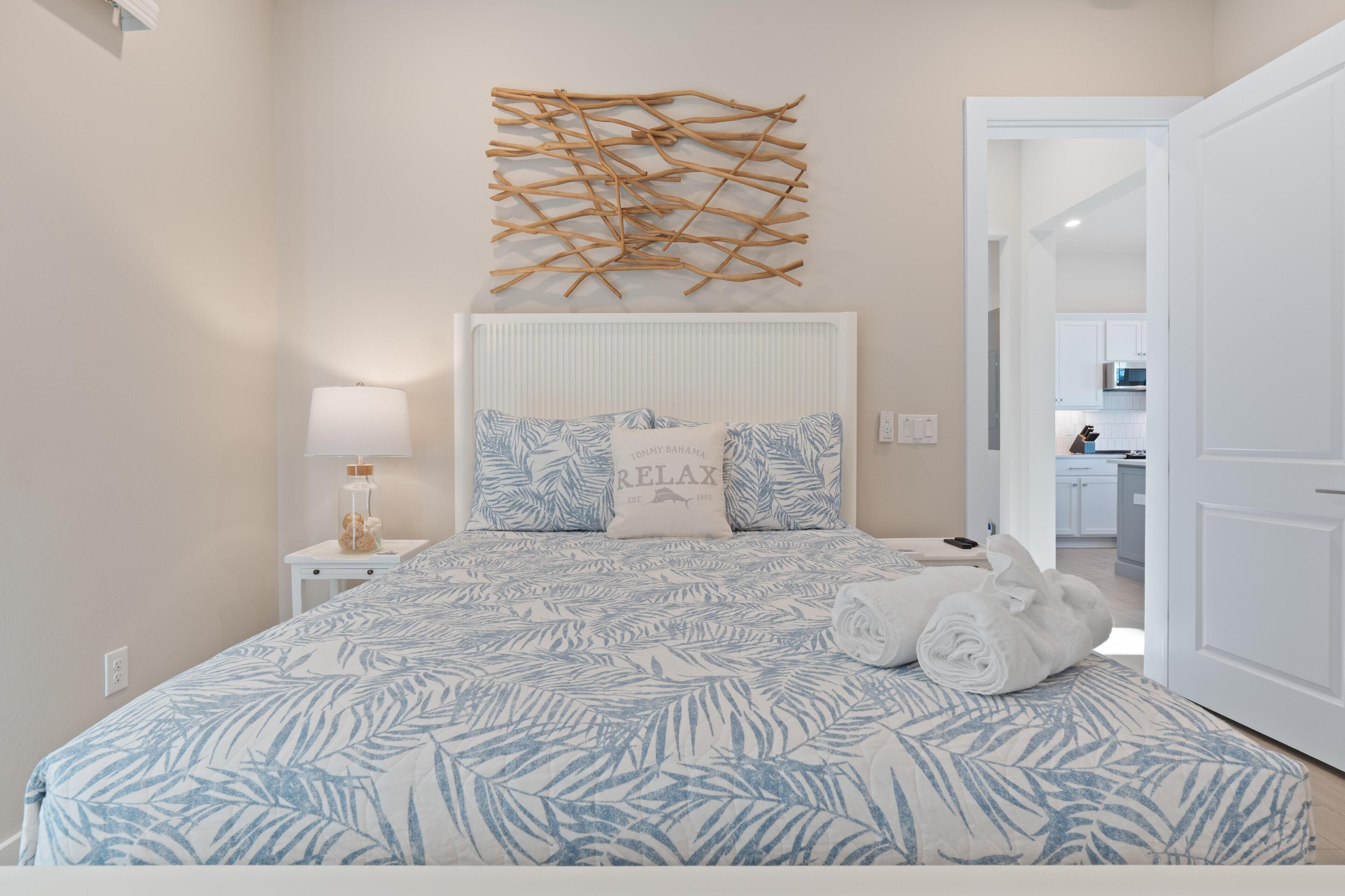 A bedroom with a bed, a nightstand, a lamp, a wall art piece, and a view of the bathroom.