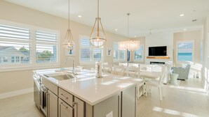 Une cuisine moderne dotée d’un îlot central, de grandes fenêtres et d’un coin repas avec des meubles blancs.