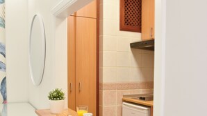 A compact kitchen with a wooden countertop, two plates with croissants, a glass of orange juice, and a small potted plant.