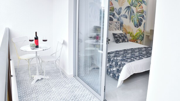 A modern bedroom with a bed, a small table with a bottle and glasses, a chair, and a glass door leading to a balcony.