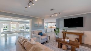 A spacious living room with a beige sofa, a wooden coffee table, and a flat-screen TV mounted on the wall. - High Tide Hideaway (Fort Myers Beach)