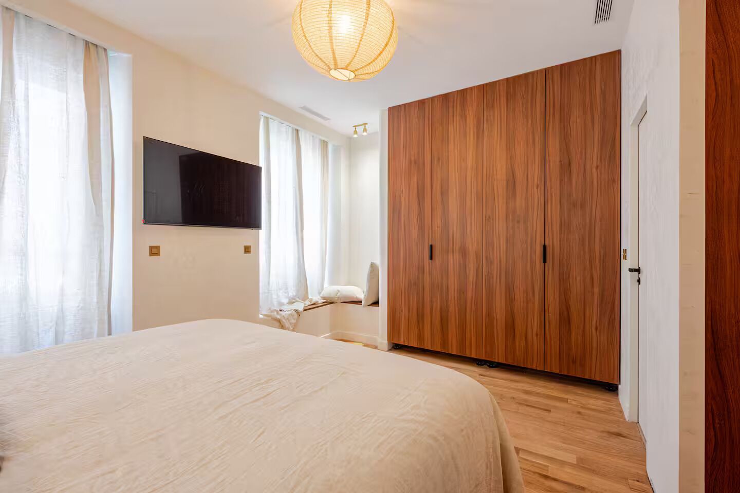 Un dormitorio con una cama grande, un armario, un televisor montado en la pared y una lámpara en el techo.