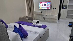 Et moderne hotelværelse med en stor seng, et fladskærms-TV monteret på væggen, et lille skrivebord og et siddeområde.
