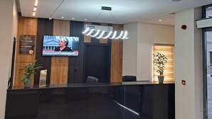 Et moderne receptionsområde med sort skranke, et fjernsyn monteret på væggen og et loft med indbygget belysning.
