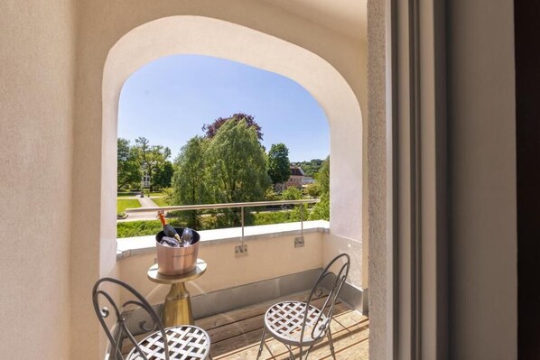 Ein Balkon mit Tisch und Stühlen, Blick auf Grünflächen und ein Gebäude in der Ferne.