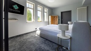 Ein Hotelzimmer mit Bett, Kleiderschrank, Schreibtisch und Fernseher, der den Namen des Hotels zeigt.