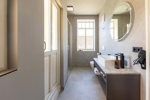 Ein modernes Badezimmer mit einem großen Spiegel, einem Waschbecken und einer Dusche.