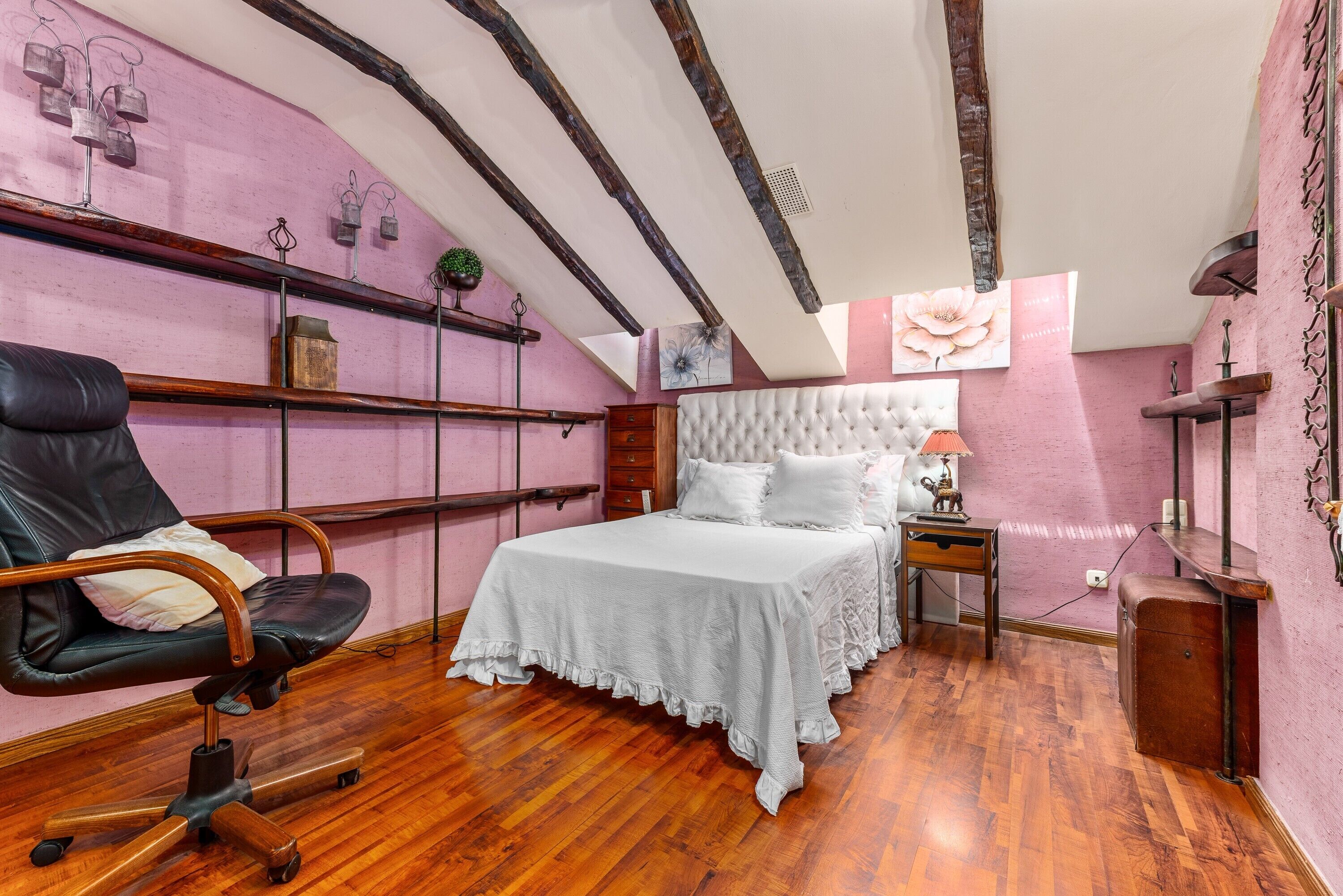 A bedroom with a bed, a chair, wooden floors, and a sloped ceiling.