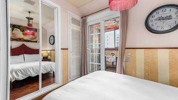 Ein Schlafzimmer mit einem Bett, einer Tür, die auf einen Balkon führt, einer Wanduhr und einer Pendelleuchte.