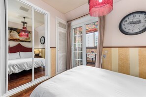 Une chambre à coucher avec un lit, une porte donnant sur un balcon, une horloge murale et un luminaire suspendu.