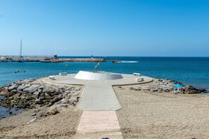 Une plage avec une structure circulaire en béton, un sentier menant à l’eau et une côte rocheuse.