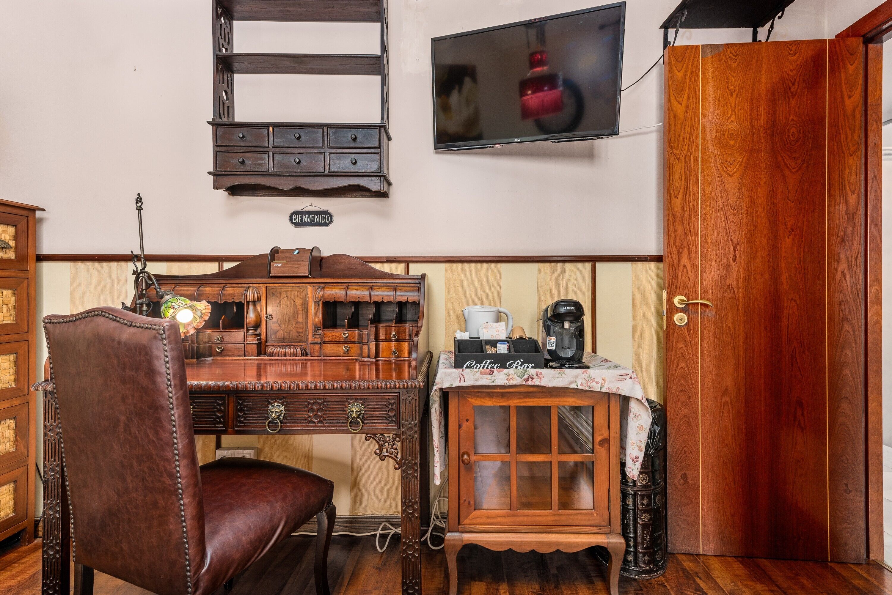 Un bureau en bois avec des tiroirs, un fauteuil en cuir, un coin café et un téléviseur fixé au mur.