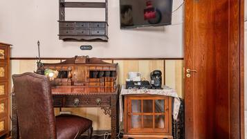 Un bureau en bois avec des tiroirs, un fauteuil en cuir, un coin café et un téléviseur fixé au mur.