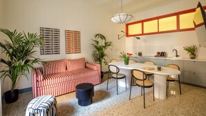 Ein modernes Wohnzimmer mit einem gestreiften Sofa, einem Esstisch mit Stühlen und einer Küchenzeile mit Fenster über der Spüle.