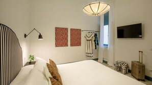Ein Hotelzimmer mit Bett, Fernseher, Lampe und Koffer.