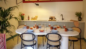 Ein Essbereich mit einem runden Tisch, gedeckt für sechs Personen, umgeben von Korbstühlen. Im Hintergrund ist eine Küchenzeile mit Spüle und Arbeitsplatte zu sehen.