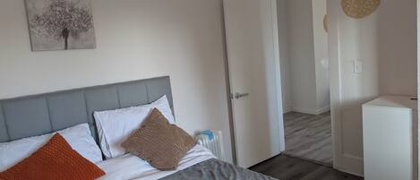 Une chambre à coucher avec un lit, une tête de lit grise, une porte blanche et une petite armoire blanche.