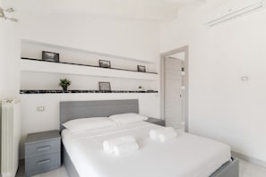 A modern bedroom with a bed, bedside tables, a radiator, and a door.