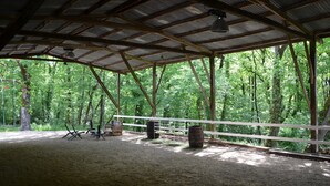 A covered outdoor area with a dirt floor, wooden benches, and metal barrels.