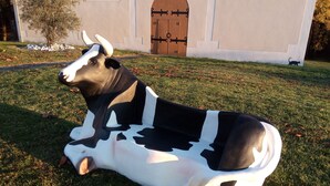 A large cow sculpture in a grassy area with a building in the background labeled "FALGADE".