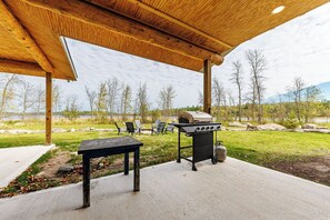 Eine Außenpatio mit Grill, Sitzgelegenheit und Blick auf einen See und Bäume.