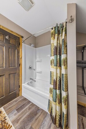 Ein Badezimmer mit einer weißen Badewanne, einer Holztür und einem Duschvorhang mit Blattmuster.