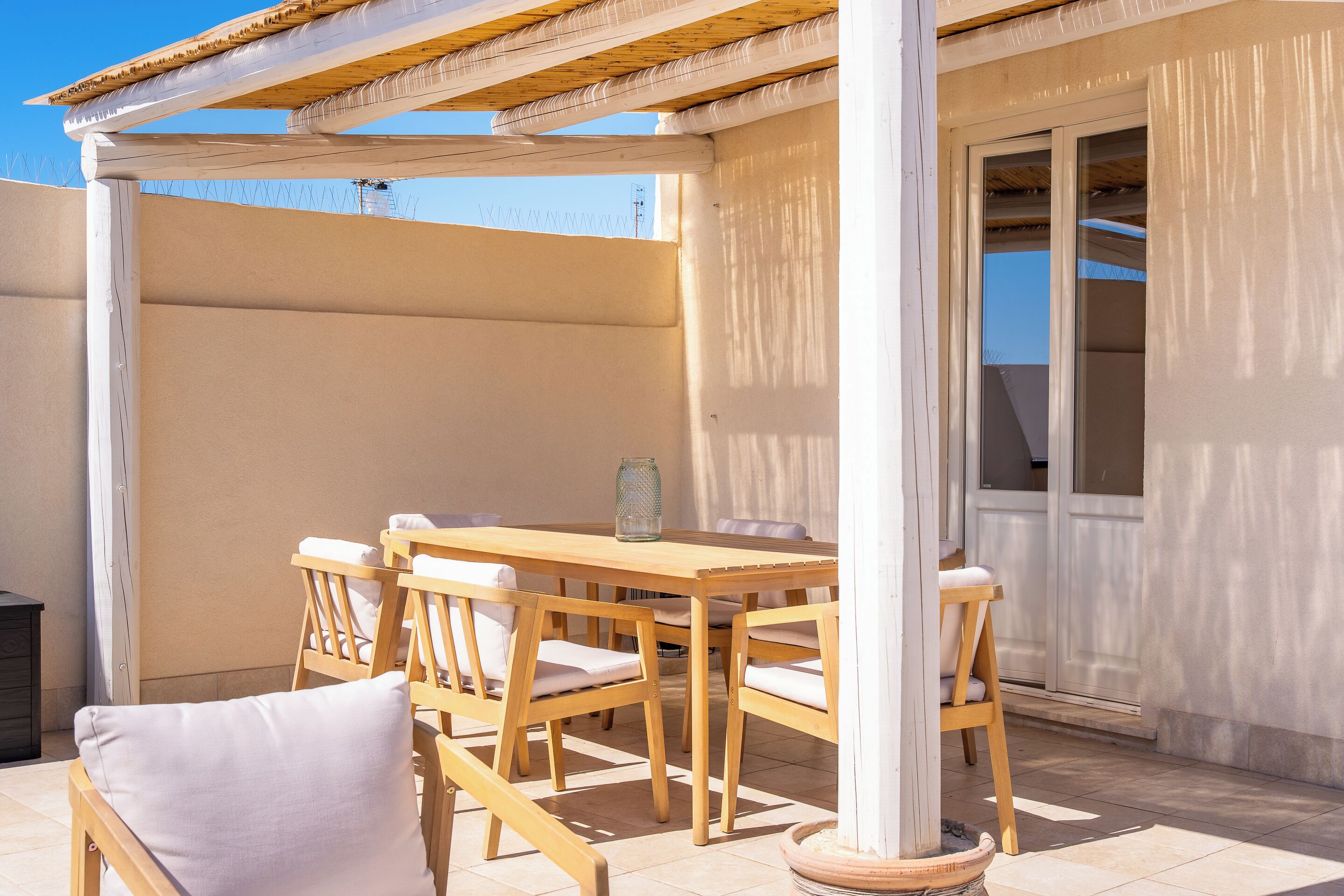 Un patio al aire libre con una mesa y sillas de madera, una planta en maceta y vistas del cielo.