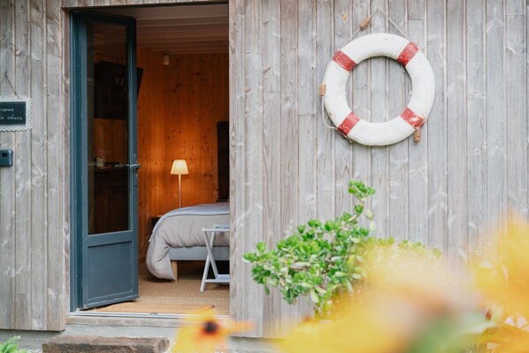 Une façade en bois avec une porte donnant sur une pièce comprenant un lit et une lampe.