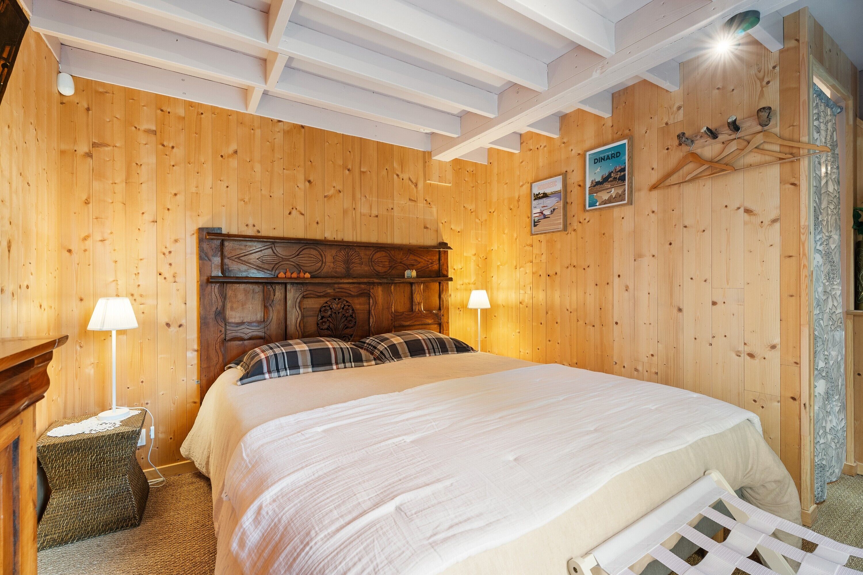 Een kamer met houten lambrisering, een bed, twee bedlampen, een kleine tafel en een kapstok aan de muur.