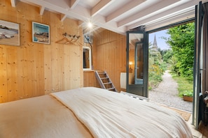 Une pièce en bois avec un lit, une échelle et une porte donnant sur un jardin.