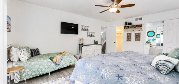 Un dormitorio con dos camas, ventilador de techo, televisor y cómoda.
