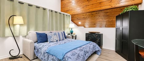 Quarto com cama, luminárias de cabeceira, teto de madeira, um armário preto e cortina verde.